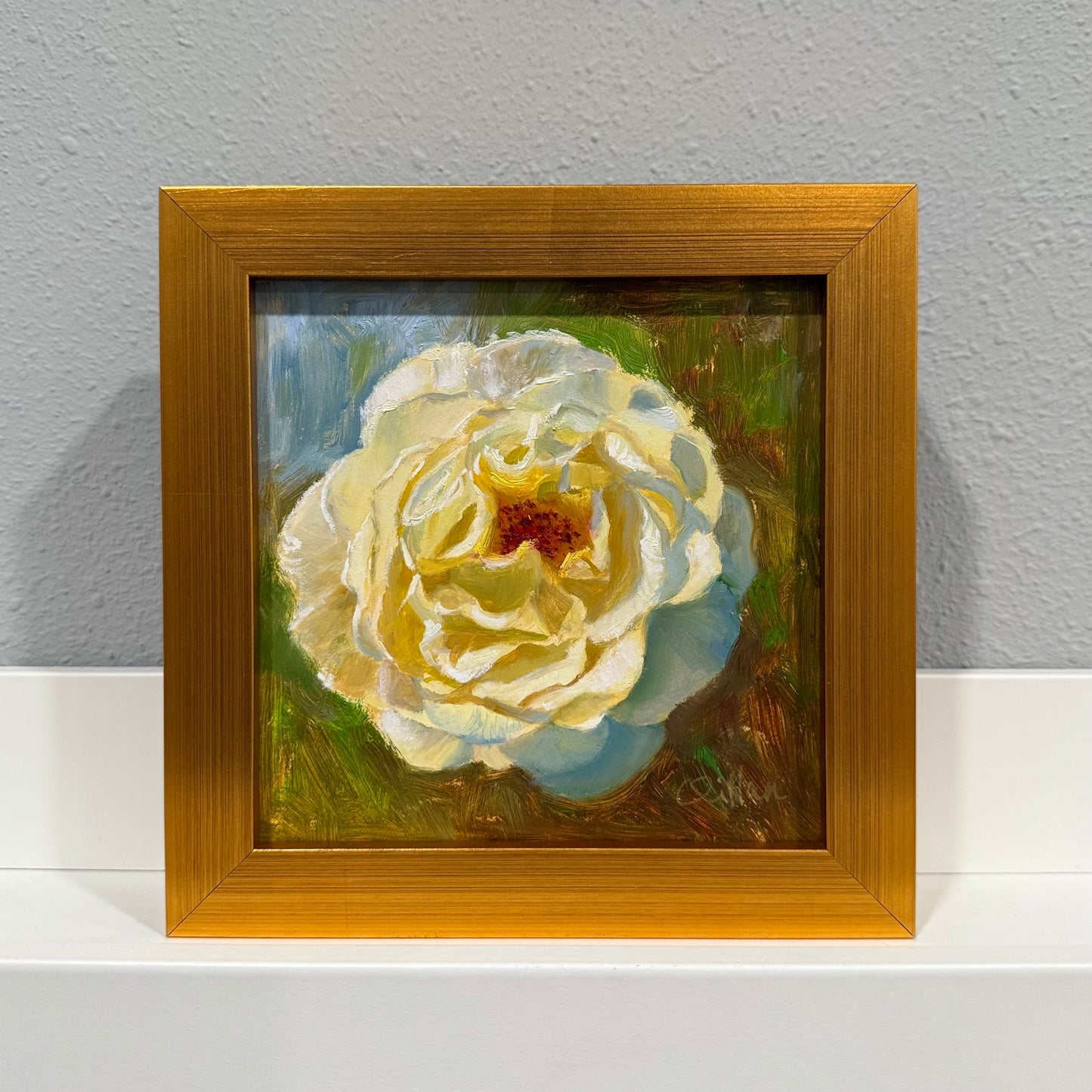 Framed painting of a white flower with a brown frame on a gray wall.