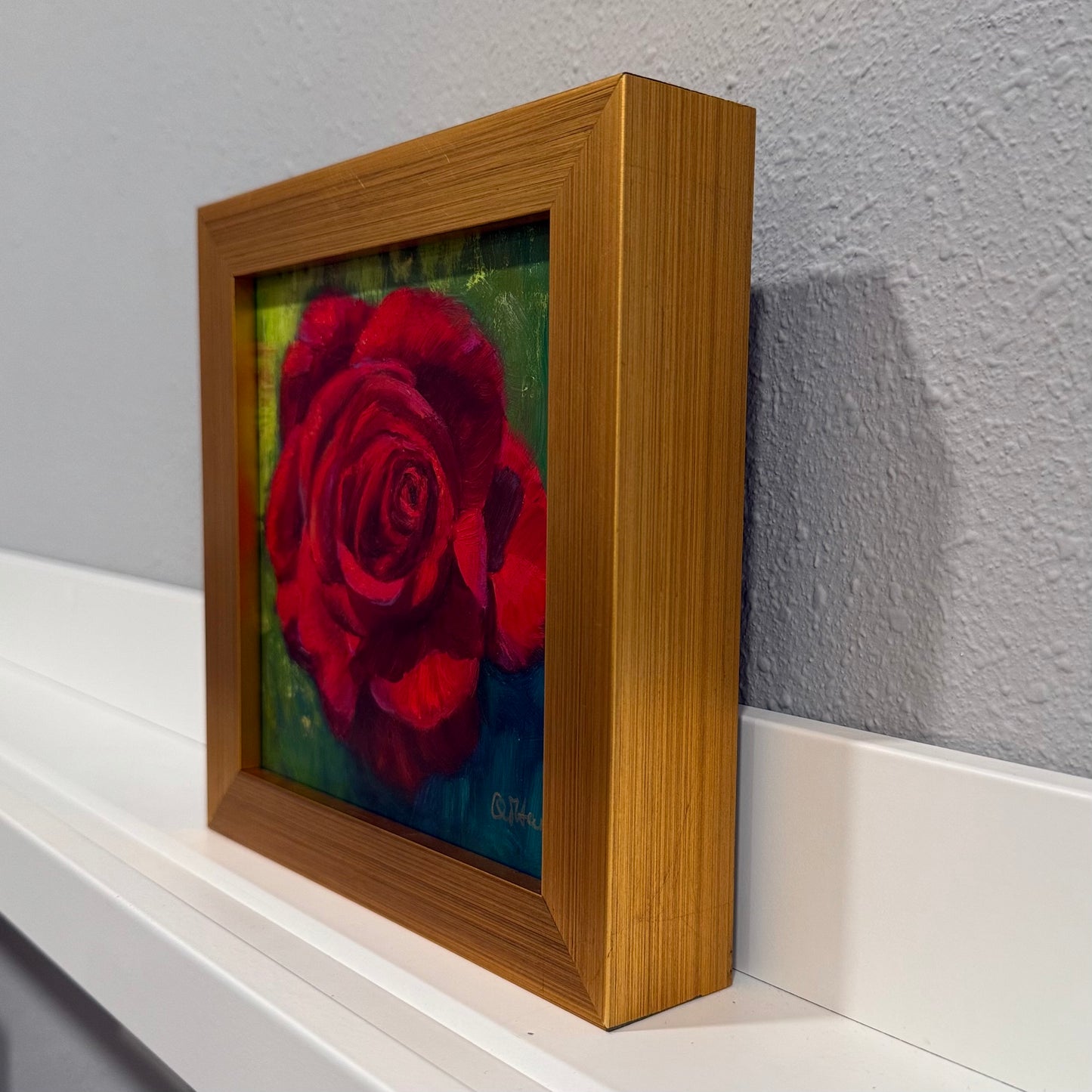 Framed artwork of a red rose on a white surface with a gray wall background