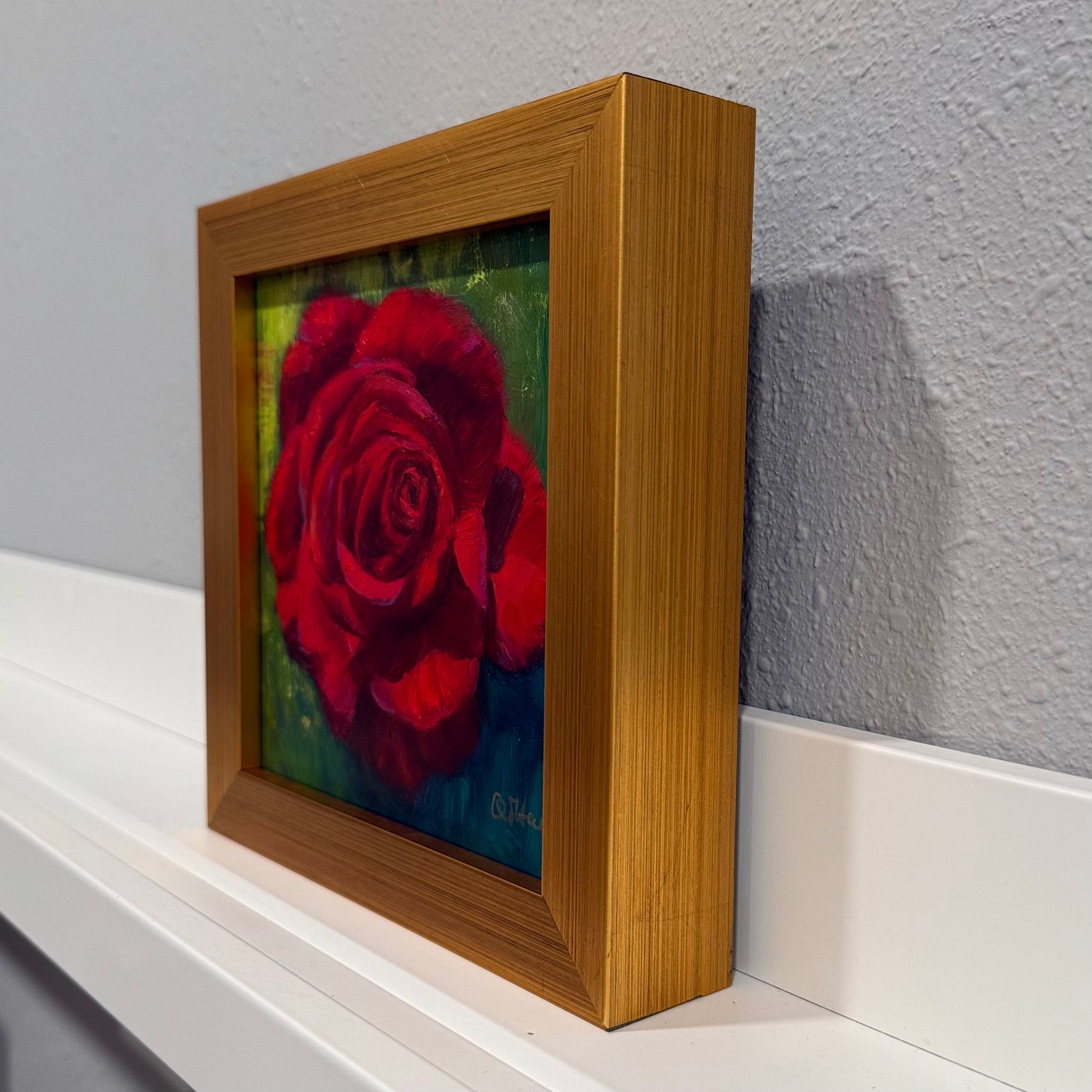 Framed artwork of a red rose on a white surface with a gray wall background