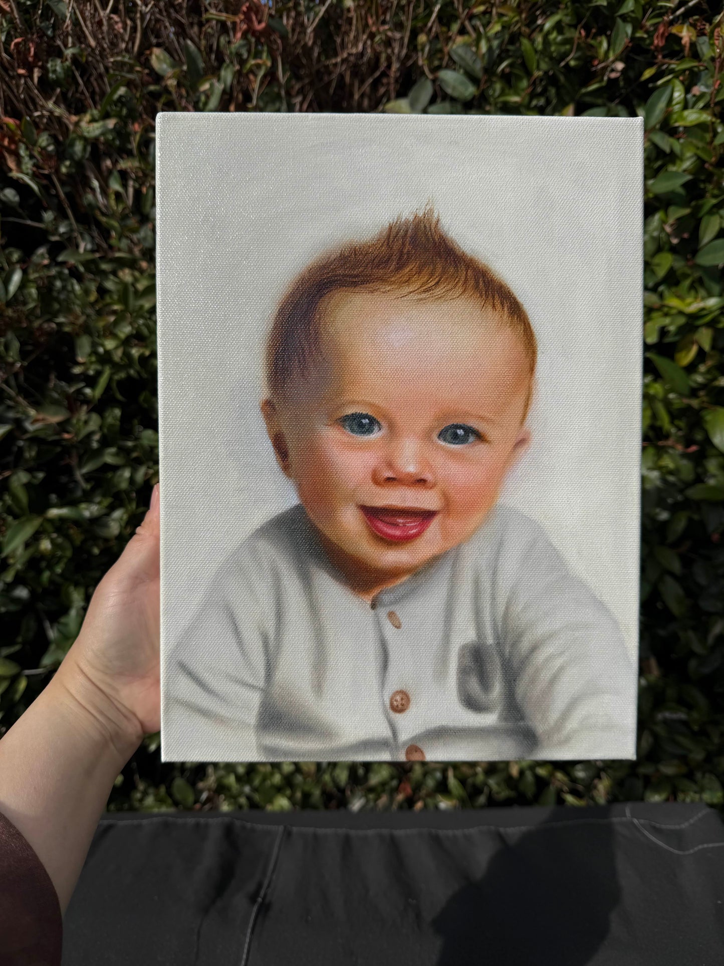 Hand holding a portrait of a smiling baby against a natural background